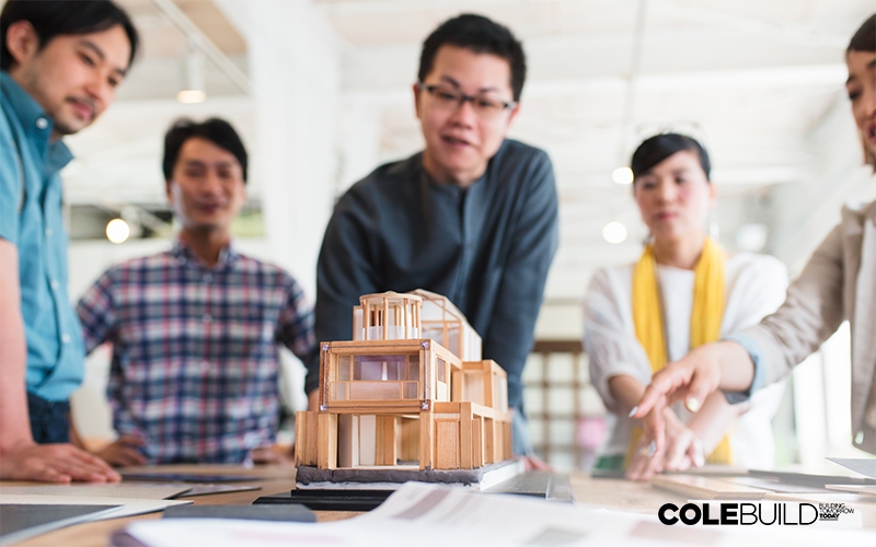 Team of architects stood around a table looking at an architectural 3D model of a building