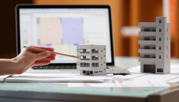 Architect hand with model building, laptop and plans