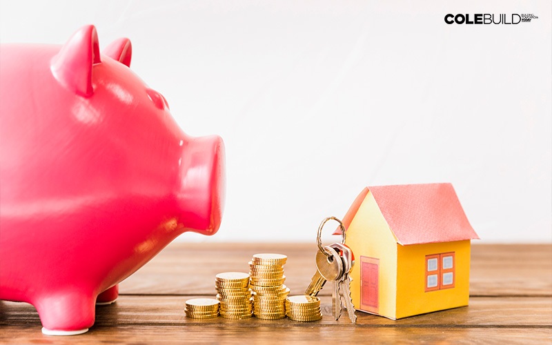 piggy bank and savings beside keys and a tiny house model