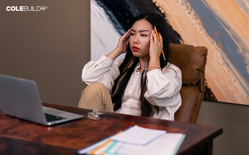 stressed woman holding her temples in front of her laptop