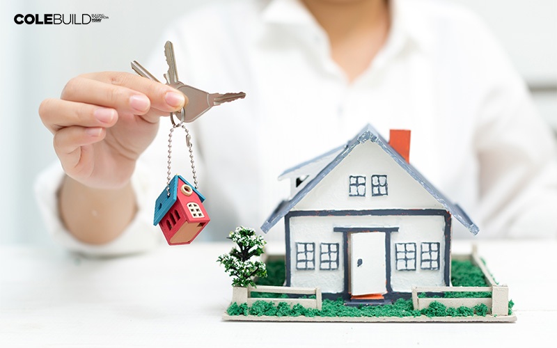 Hand with key next to house model